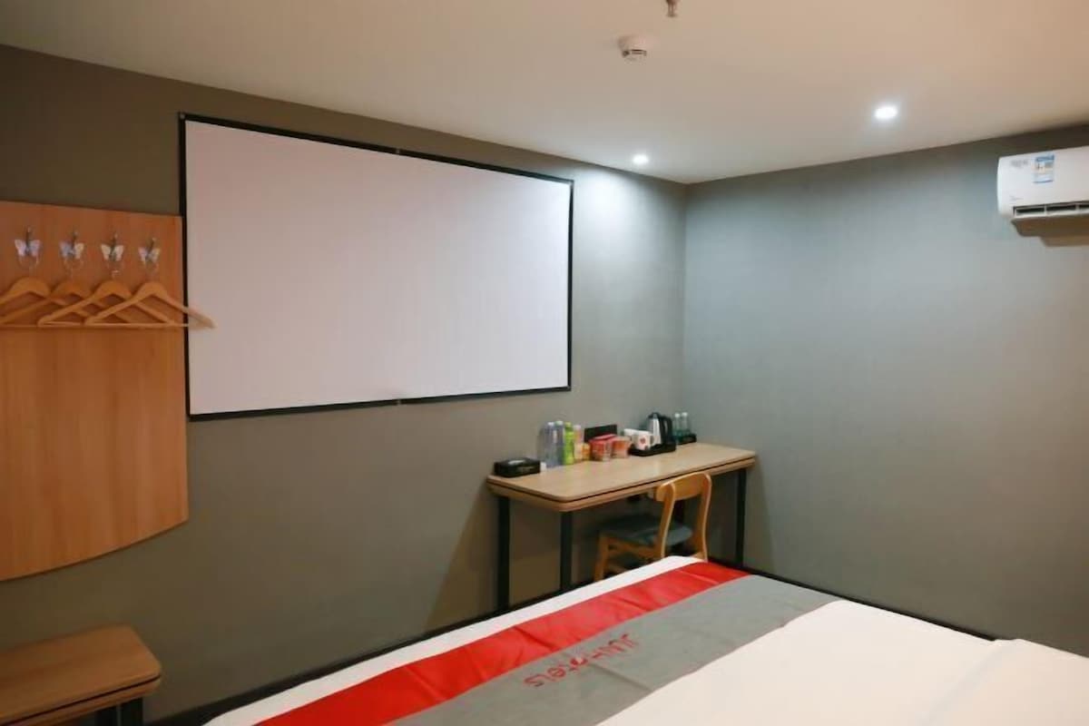 A hotel room with a bed, a desk, a chair, a wardrobe, and a projector screen.