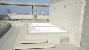 A rooftop terrace with two hot tubs, a view of the city skyline, and a modern architectural design. - Distrito 90 by Wellcome (Barranquilla)