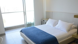 A hotel room with a bed, a nightstand, a chair, and a large window. - Distrito 90 by Wellcome (Barranquilla)