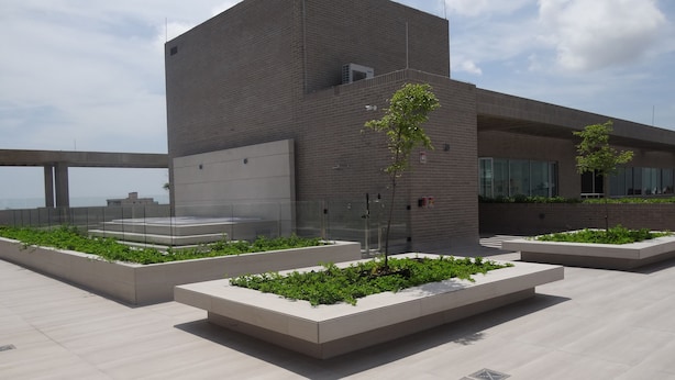 A modern building with a flat roof, rectangular planters with greenery, and a clear sky. - Distrito 90 by Wellcome (Barranquilla)