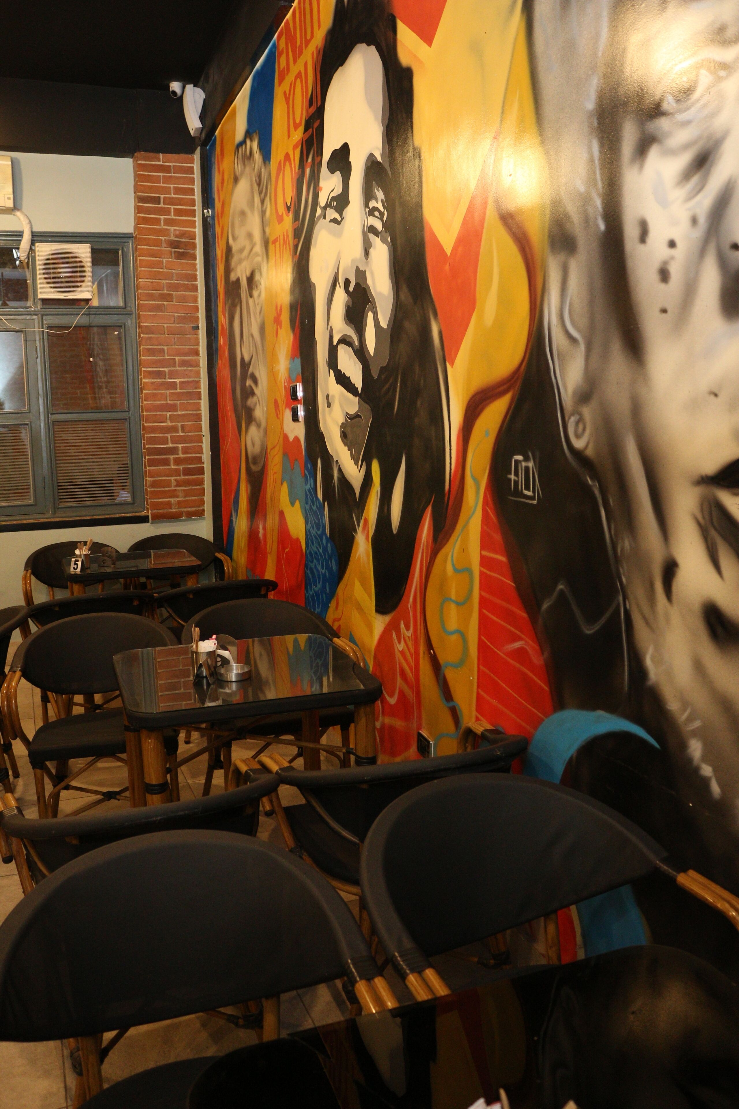 A dining area with tables and chairs, a mural with abstract art, and a brick wall.