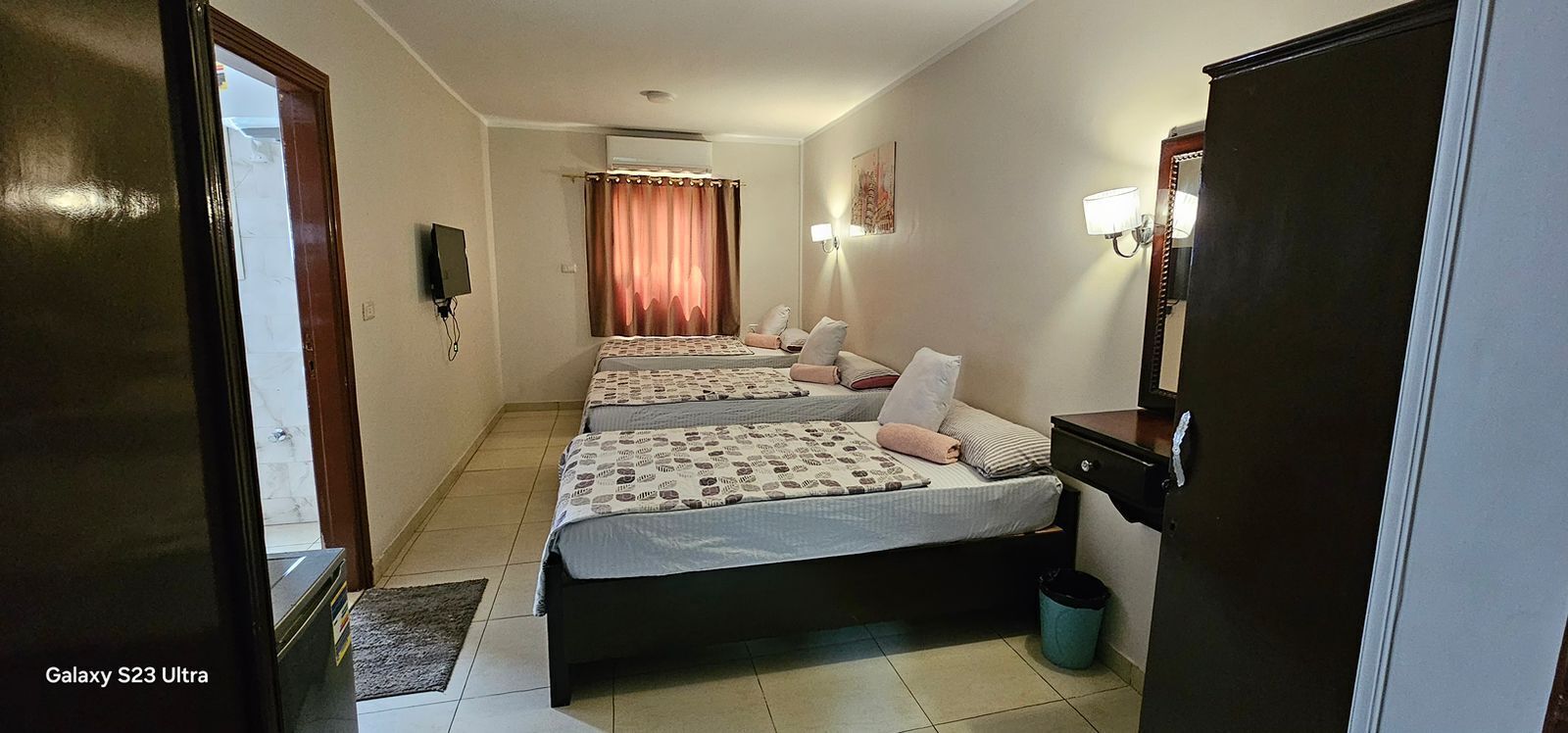 Une chambre d’hôtel avec deux lits, un bureau, un miroir et une télévision.