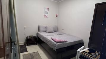 Un dormitori amb un llit, una tauleta de nit, una catifa petita, una decoració a la paret i una porta.