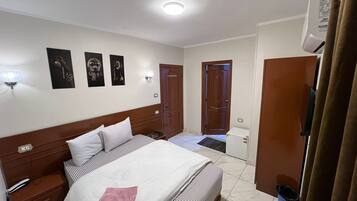 A hotel room with a bed, bedside tables, a wardrobe, and a door leading to another room.
