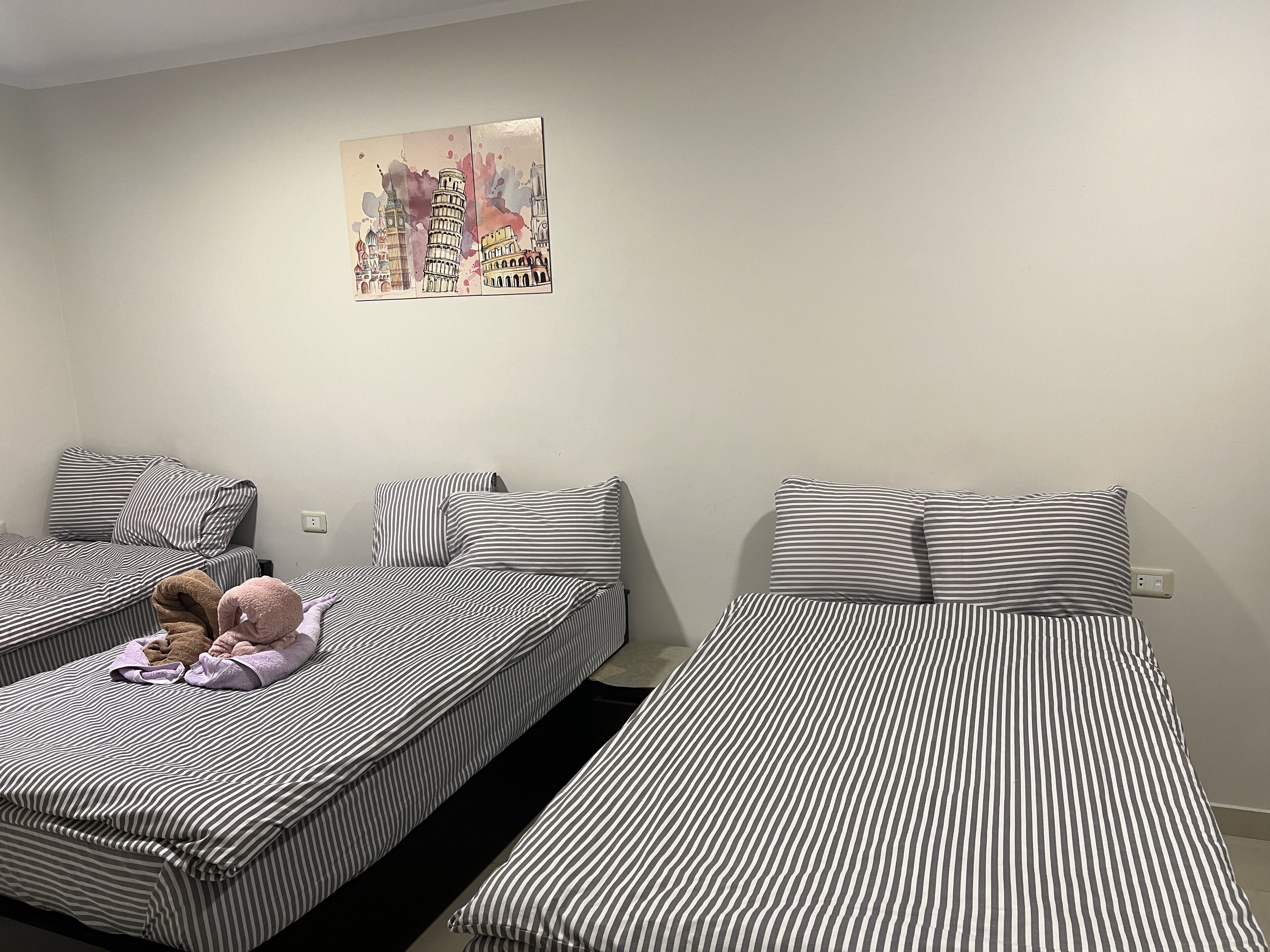 Een kamer met twee bedden, elk voorzien van gestreept beddengoed. Op de muur hangt een schilderij van bekende bezienswaardigheden.