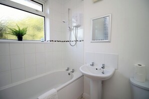 Enjoy a refreshing bath in the bathroom, featuring a bathtub, sink, and toilet, with a view of lush greenery outside.