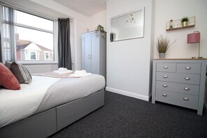 Cozy retreat with a neatly made bed, grey wardrobe, and a bedside table with a lamp.