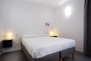 Ein ordentlich eingerichtetes Schlafzimmer mit einem Bett, zwei Nachttischen mit Lampen, einem kleinen Wandbild und einer Steckdose.