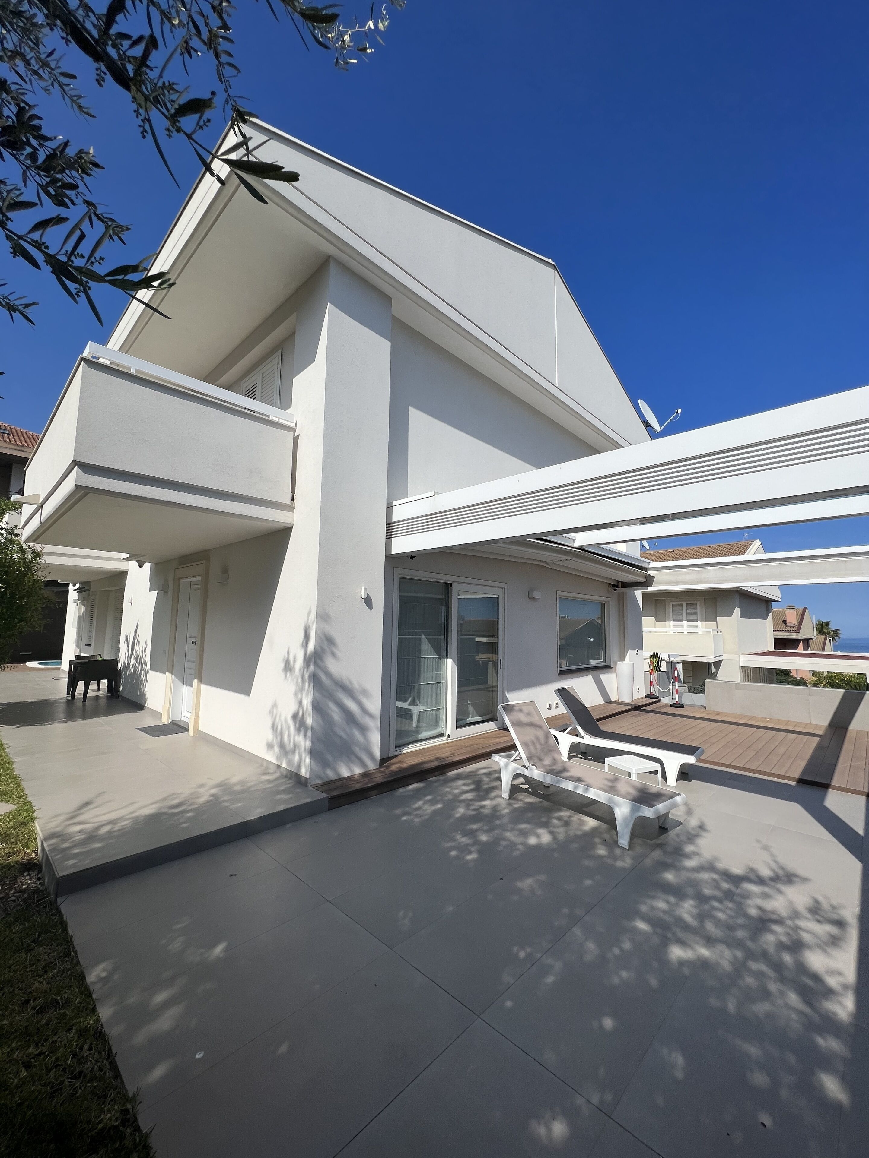 A modern two-story house with a covered patio area, a sliding glass door entrance, and a view of the ocean.