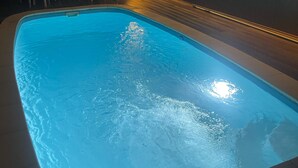 A swimming pool with a clear blue water surface, surrounded by lounge chairs and a wall with a recessed light fixture.
