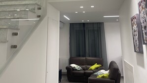 A modern living room with a staircase, two leather sofas, and a large window with curtains.