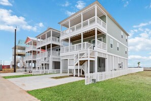 A multi-story beachfront house with balconies, a white picket fence, and a clear sky. - Sunkissed Starfish: Heated Pool & Spa, beach access, Galveston (Galveston)