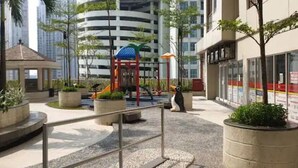 A playground with slides and a climbing structure, surrounded by planters and a gazebo.