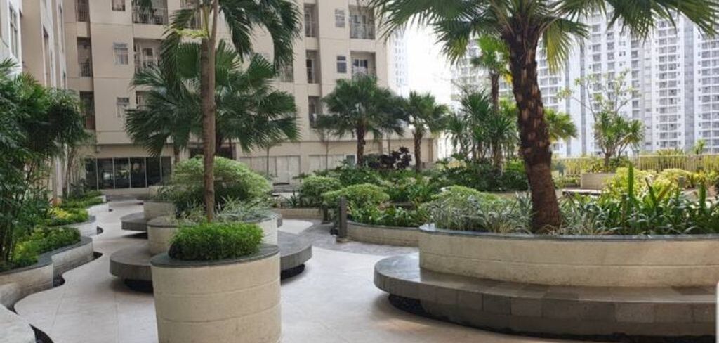 A courtyard with circular planters and palm trees, surrounded by high-rise buildings.