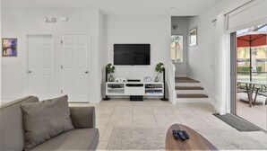 Een moderne woonkamer met een flatscreen televisie, witte muren en een trap naar een balkon.