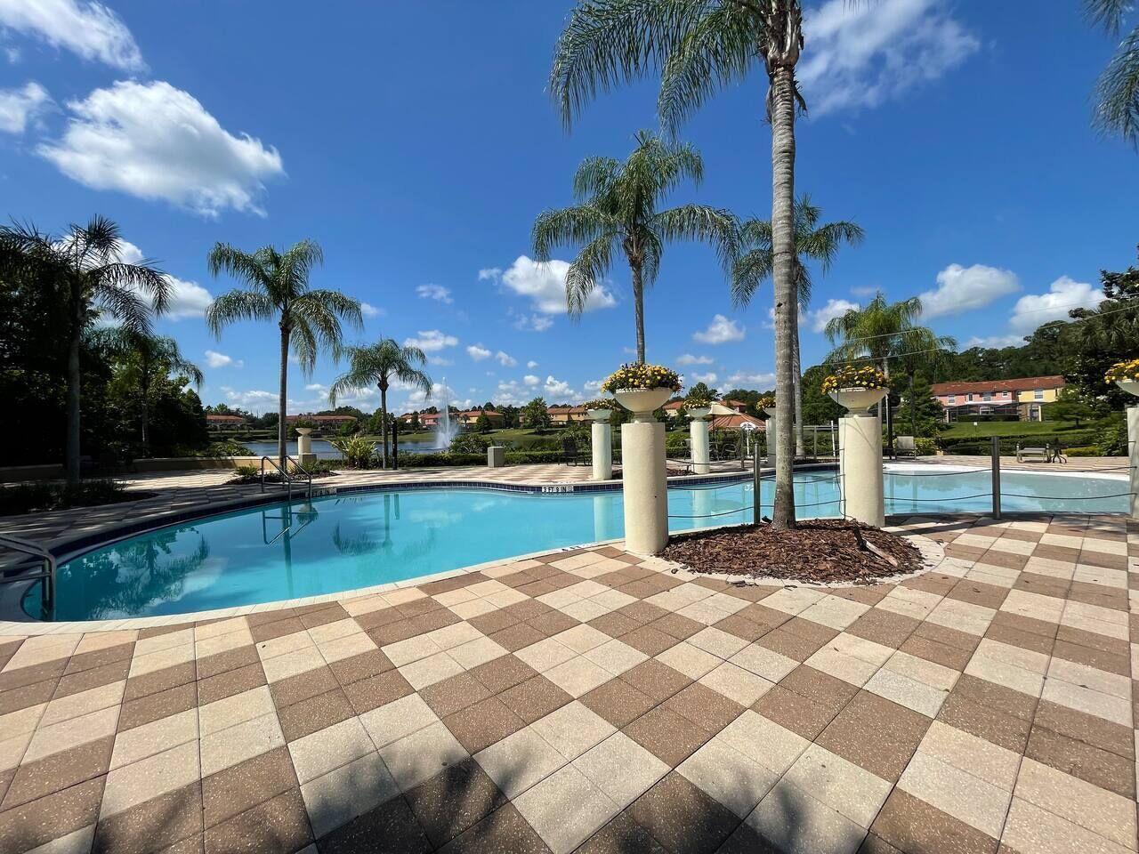 Una piscina con suelo de baldosas de diseño ajedrez, rodeada de palmeras y un cielo azul despejado.