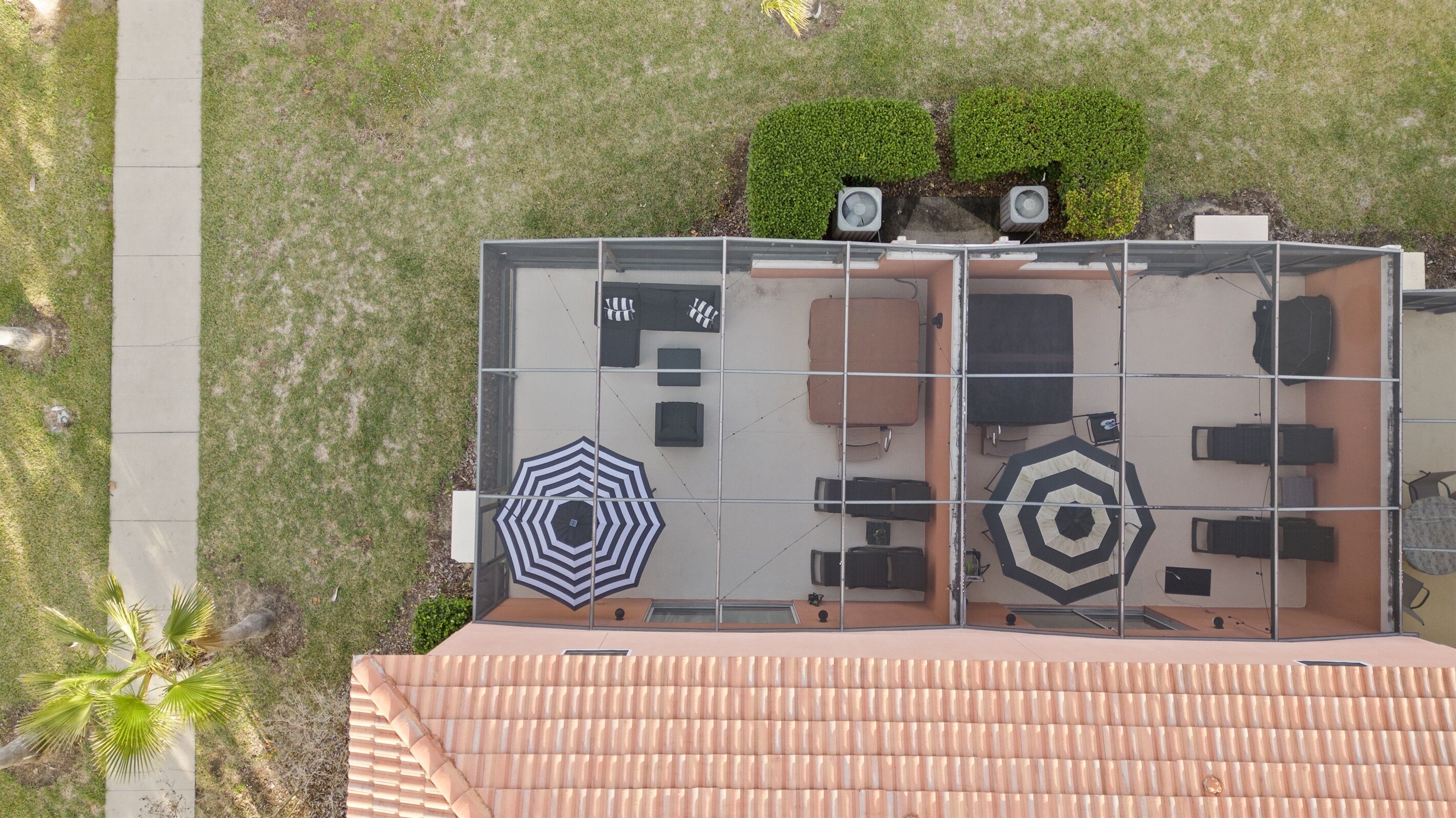 A rooftop terrace with a tiled floor, two air conditioning units, a small garden area, and a seating arrangement with a patterned umbrella.