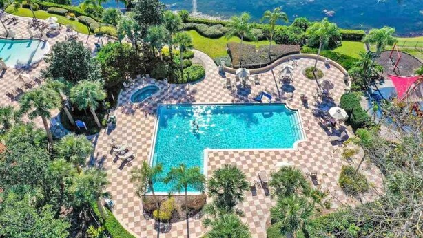 Luchtbeeld van een resort met een centraal zwembad, omringd door geruite terrassen, palmbomen en loungegedeeltes.