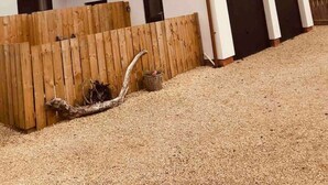 Una casa a due piani con tetto spiovente, recinzione in legno e vialetto sterrato.