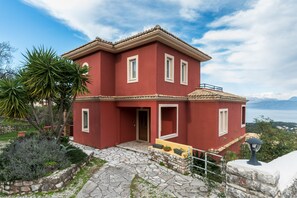 A two-story house with a red facade, stone pathway, and a view of the sea. - The Hillside Villas, Stunning Views & Private Pool (Corfu)