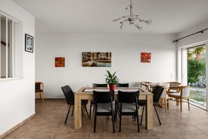 A dining area with a wooden table, black chairs, and a potted plant. There are three paintings on the wall and a chandelier above. - The Hillside Villas, Stunning Views & Private Pool (Corfu)