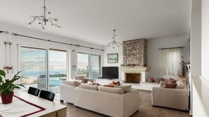 A spacious living area with a large sofa, a dining table, and a fireplace. - The Hillside Villas, Stunning Views & Private Pool (Corfu)