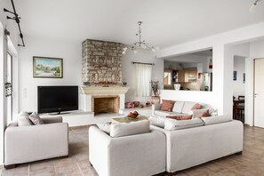 A living room with a stone fireplace, a flat-screen TV, and a sofa set. - The Hillside Villas, Stunning Views & Private Pool (Corfu)