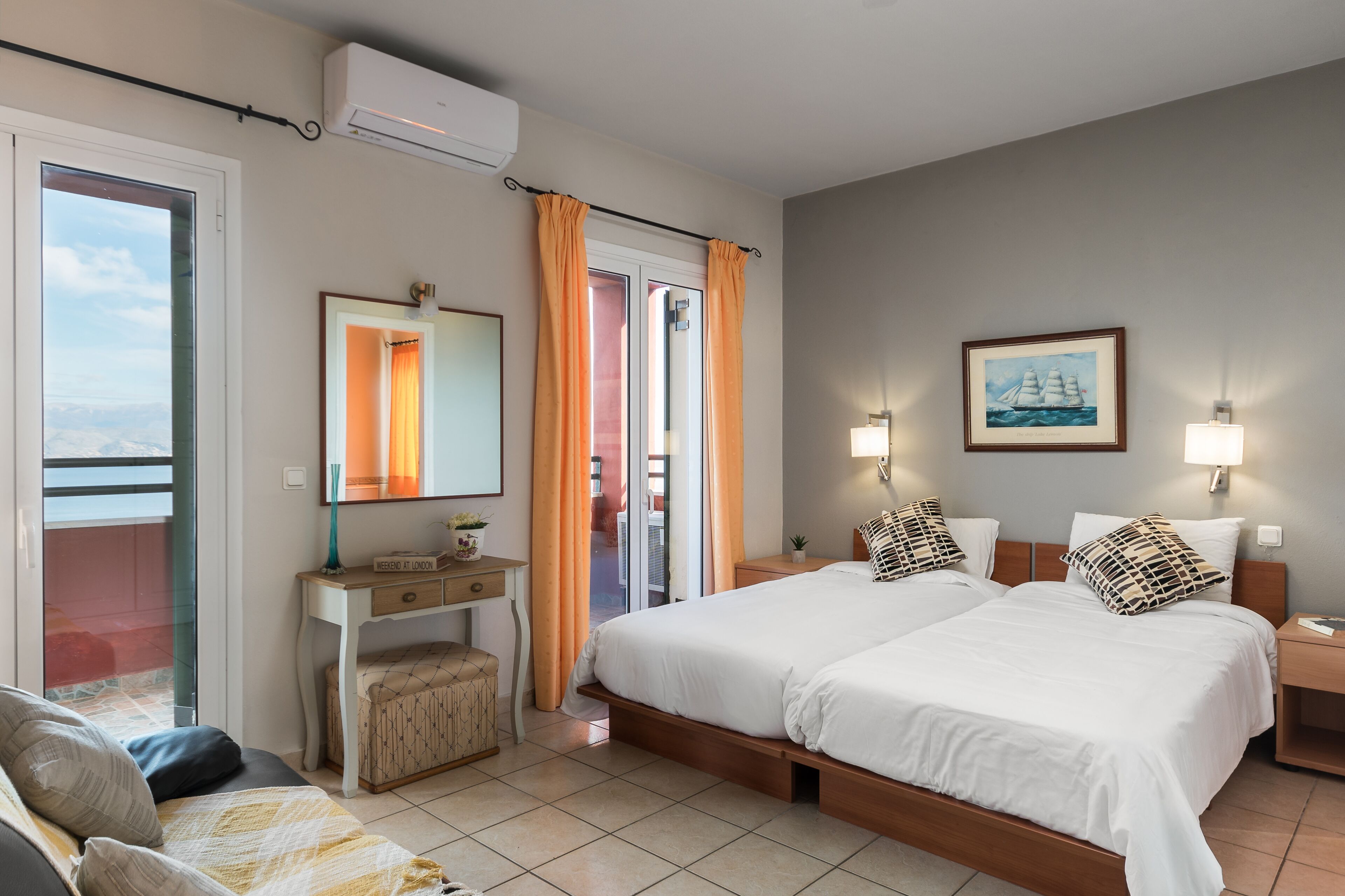 Hotelkamer met twee bedden, een bureau, een stoel en een balkon met oranje gordijnen.