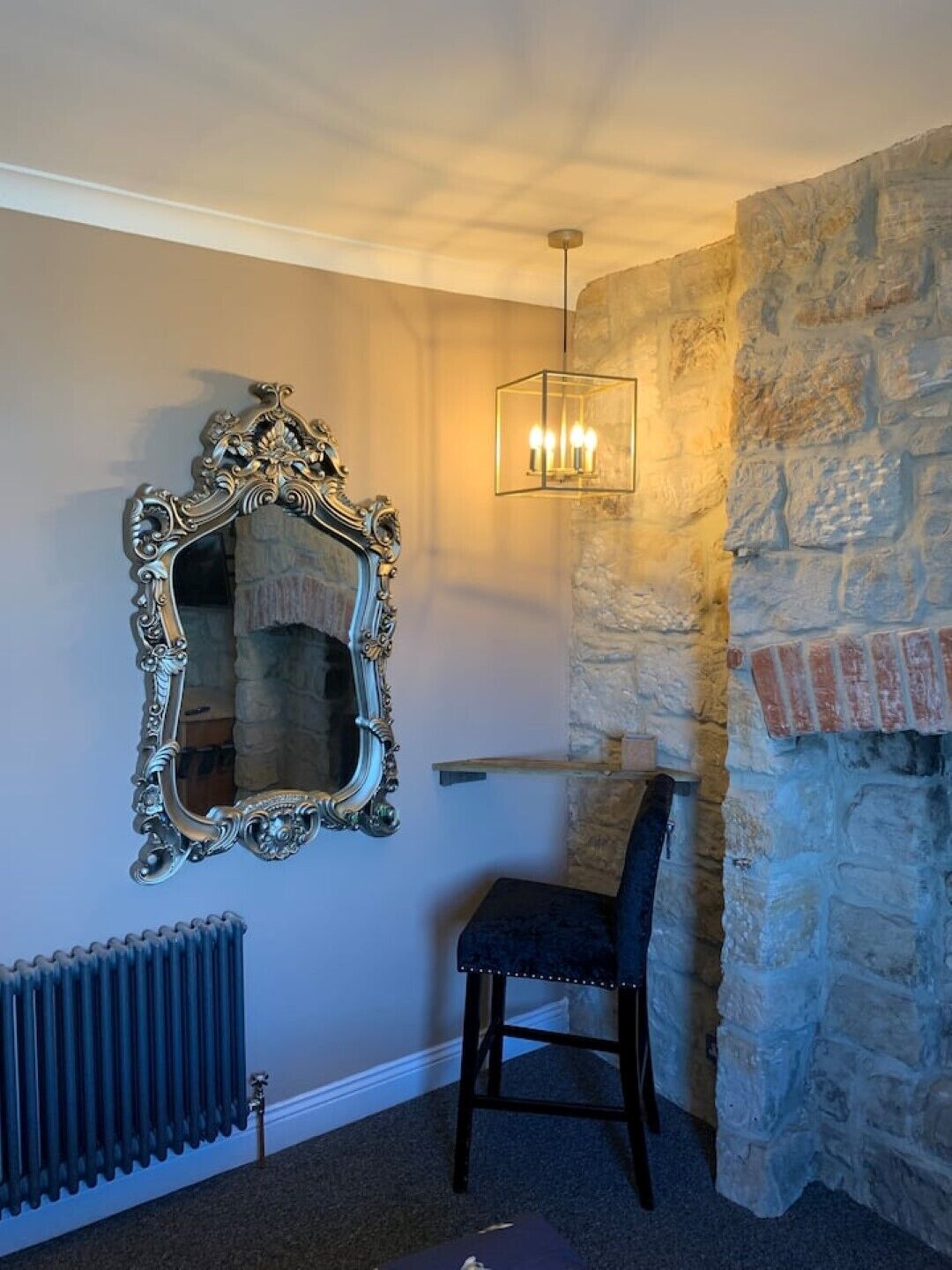 A room with a stone wall, a radiator, a chair, and a mirror with an ornate frame.