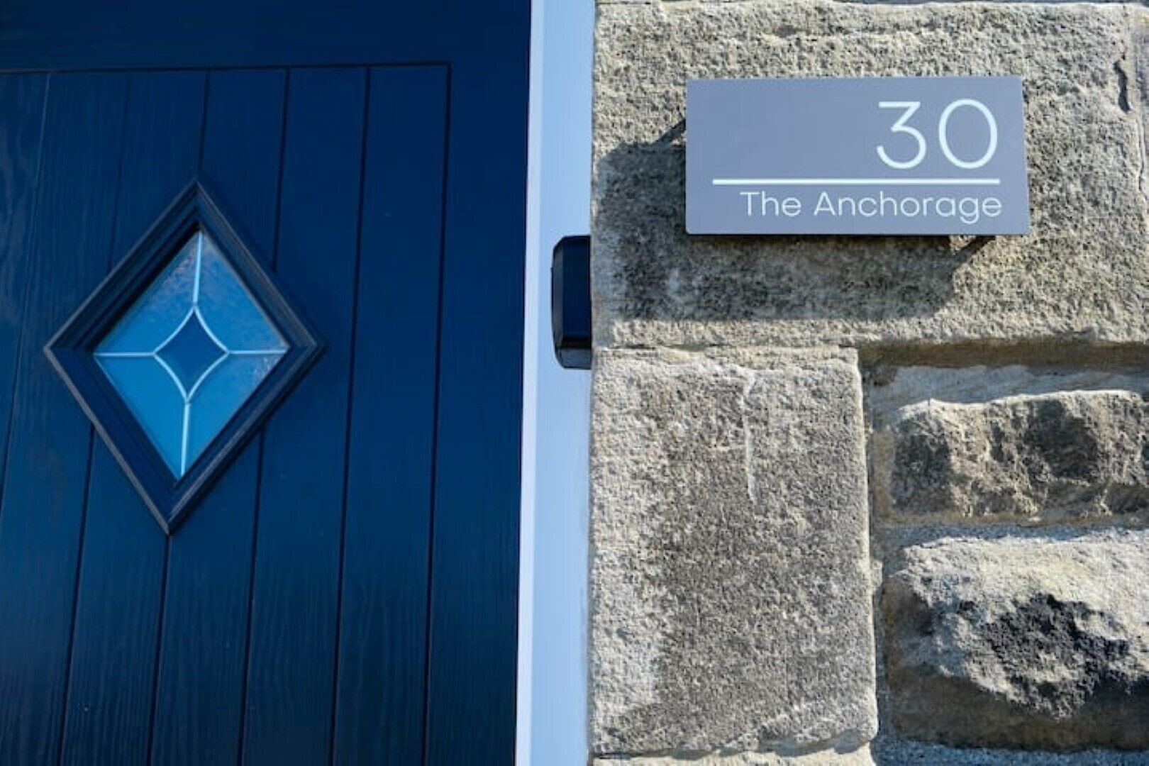 A blue door with a geometric glass window and a stone wall with a sign reading "30 The Anchorage".