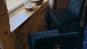 A room with a stone wall, a window overlooking a parking area, and a blue chair with a cushion. - The Anchorage - sea views and beach on doorstep (Amble)