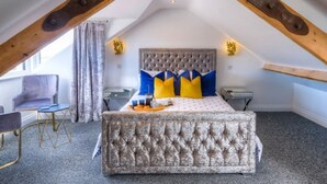 A bedroom with a vaulted ceiling, a tufted headboard, a bed with blue and yellow pillows, a bedside table, and a chair. - The Rockpool - Private HOT TUB + Sea Views (Amble)