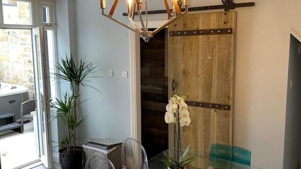 A dining area with a glass table, clear chairs, and a wooden centerpiece. - The Rockpool - Private HOT TUB + Sea Views (Amble)