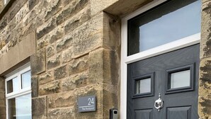 A stone building with a black door and a window. A house number '24' is visible on the wall. - The Rockpool - Private HOT TUB + Sea Views (Amble)