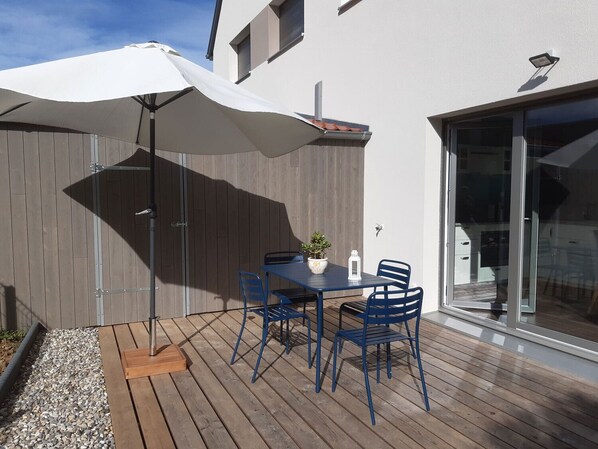 Une terrasse extérieure avec une table et des chaises, un parasol blanc et une plateforme en bois.