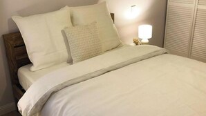 A neatly made bed with white linens and pillows, a wooden headboard, and a bedside lamp.
