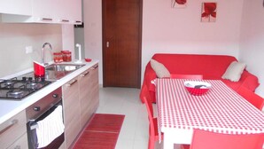 Una cocina pequeña con estufa, lavamanos y armarios, un sofá rojo con mantel a cuadros y una alfombra roja.