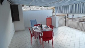 Un pequeño espacio exterior con comedor, mesa y sillas, un porche cubierto y vistas a la ciudad.