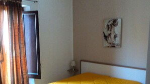 Una habitación con una cama, un cuadro en la pared, una ventana con cortinas y una puerta.