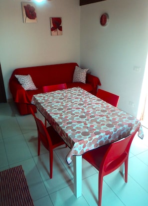 A dining area with a table covered in a polka dot tablecloth, red chairs, a red sofa with patterned cushions, and a red rug on the floor.
