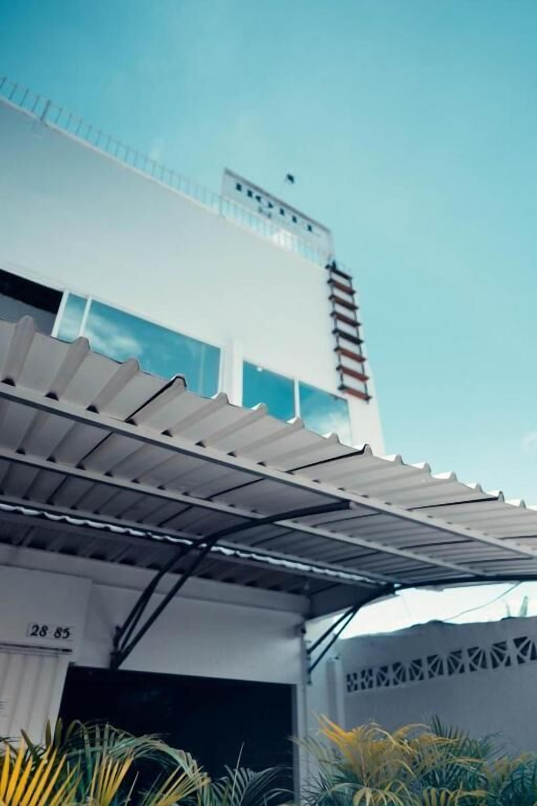 Un edificio moderno con tetto piatto, un patio coperto con tettoia in metallo e una parete esterna bianca.