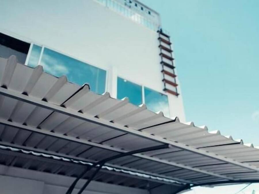 Un edificio moderno con tetto piatto, un patio coperto con tettoia in metallo e una parete esterna bianca.