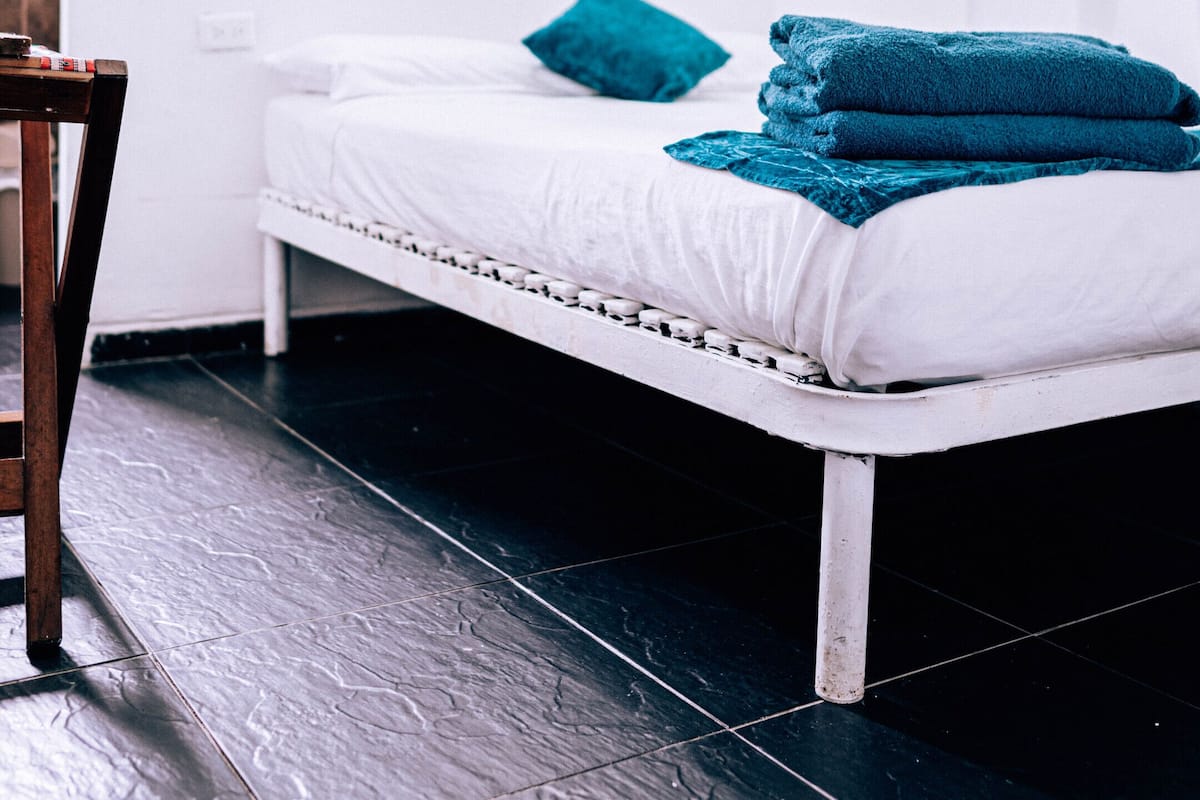 Un dormitorio con cama, mesita de noche, un cuadro en la pared y ventana con cortinas.