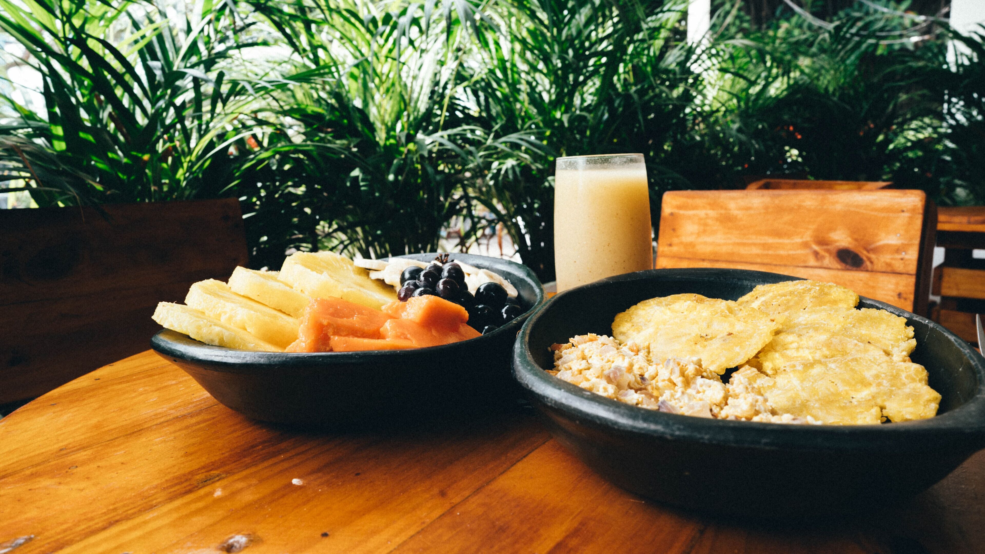 A wooden table with two bowls of food, one containing sliced fruit and the other with a creamy dish, and a glass of a light-colored beverage.