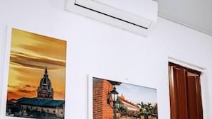 Una habitación con un equipo de aire acondicionado blanco montado en la pared, dos cuadros enmarcados que muestran escenas arquitectónicas y una puerta de madera.