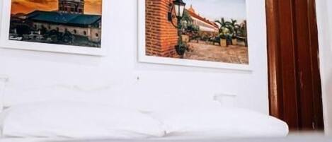 A room with a white air conditioning unit mounted on the wall, two framed pictures depicting architectural scenes, and a wooden door.