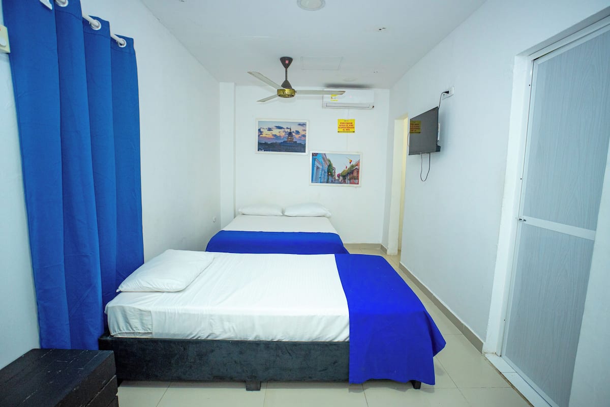Una habitación con dos camas, ventilador de techo, televisor montado y una puerta.