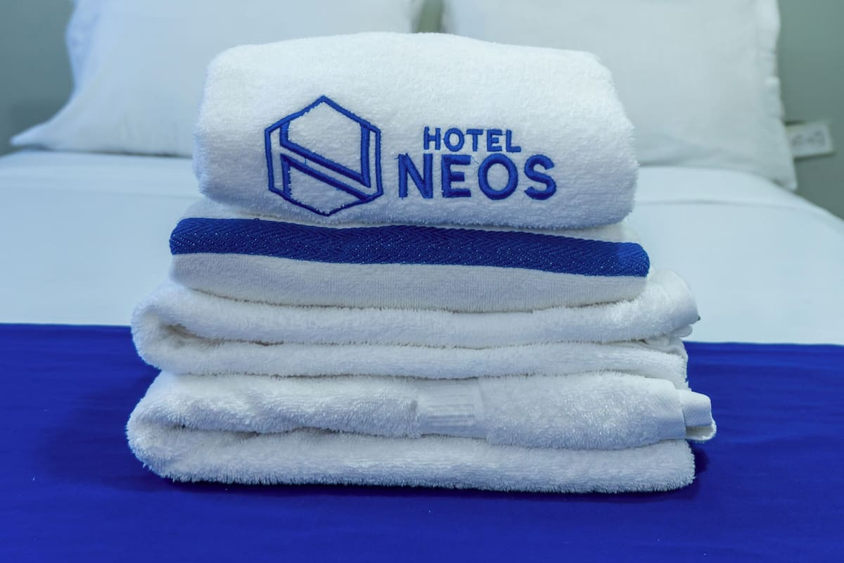 Un montón de toallas blancas con un logotipo sobre una cama en una habitación de hotel.