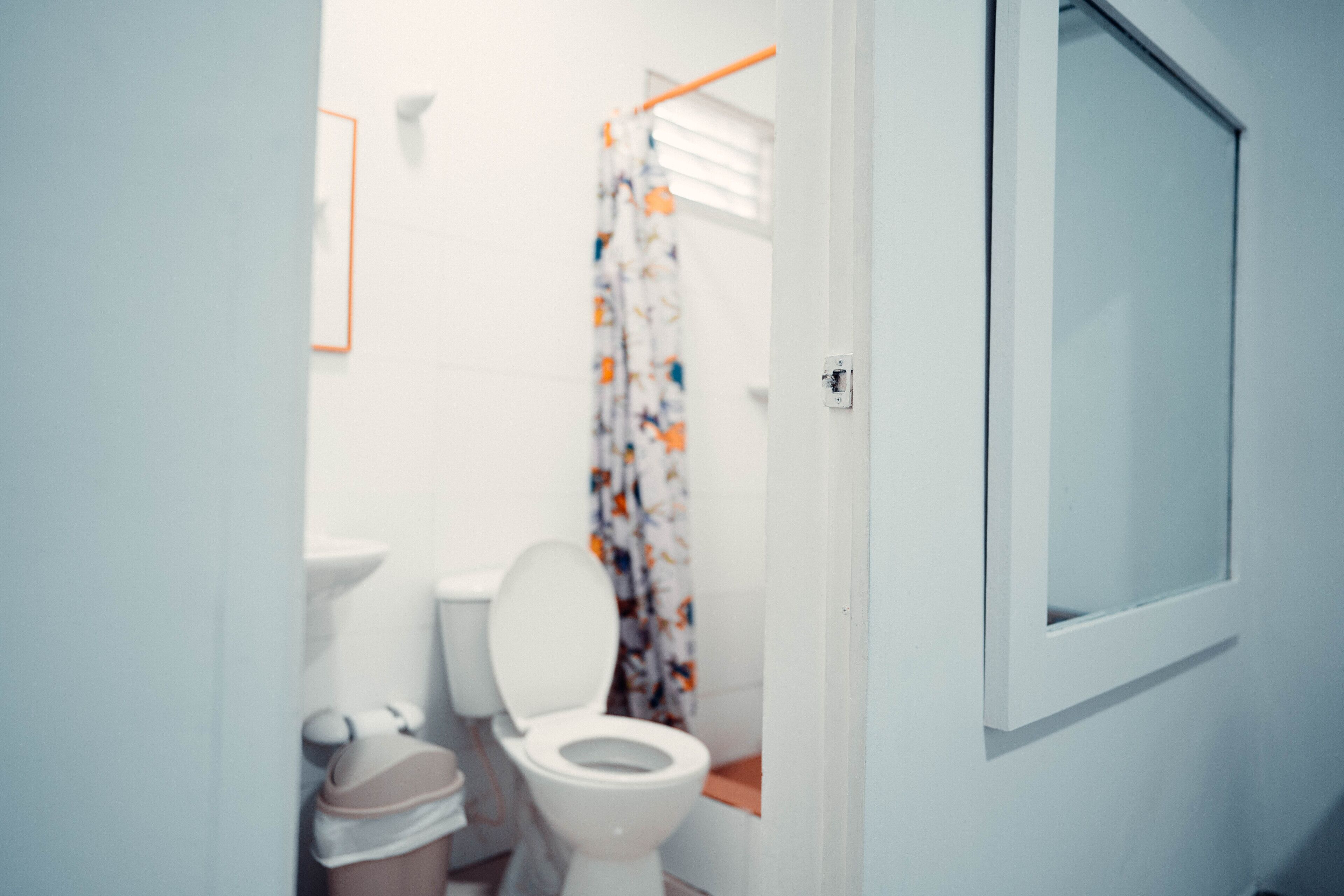 Un baño pequeño con inodoro, un cubo de basura y cortina de ducha.