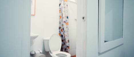 A small bathroom with a toilet, a trash bin, and a shower curtain.